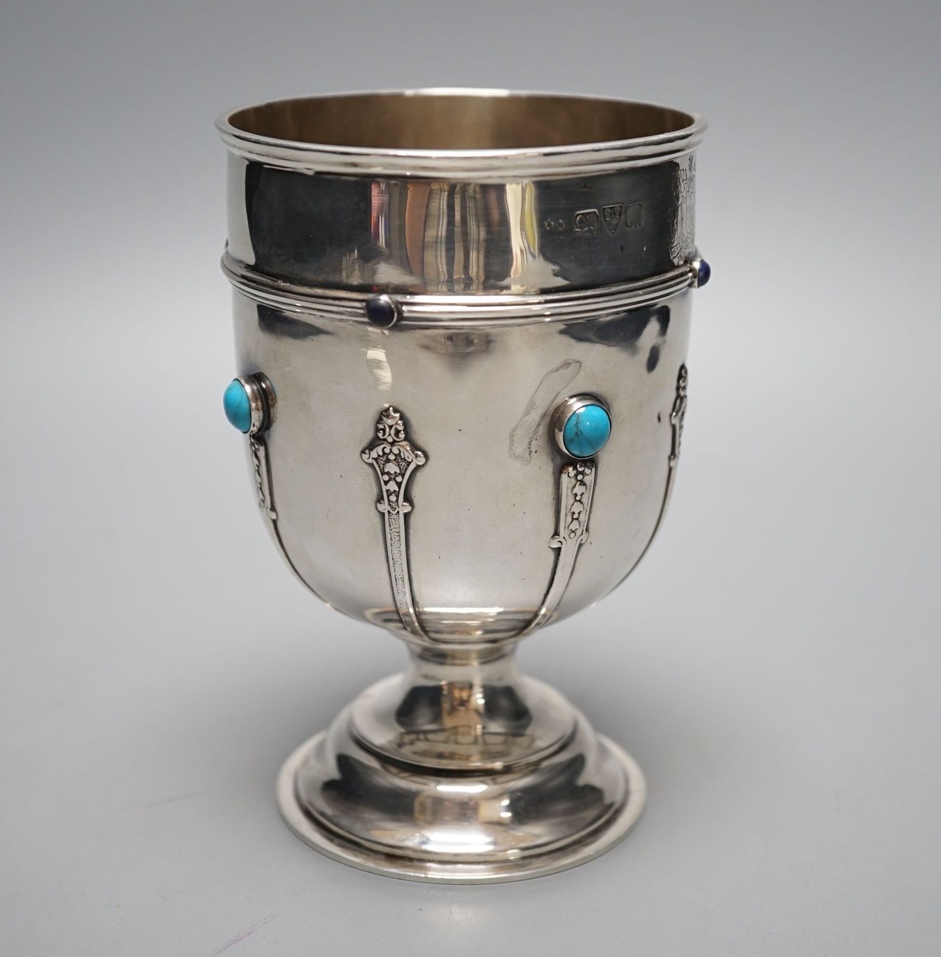 A George V silver goblet or pedestal cup with inset cabochon turquoise and cabochon lapis lazuli, with engraved crest and strapwork decoration, Henry Moreton, Chester, 1913, 13.6cm, gross weight 7oz.